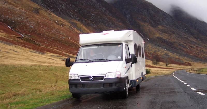 Camping-car roulant sur une route humide à travers des collines brumeuses