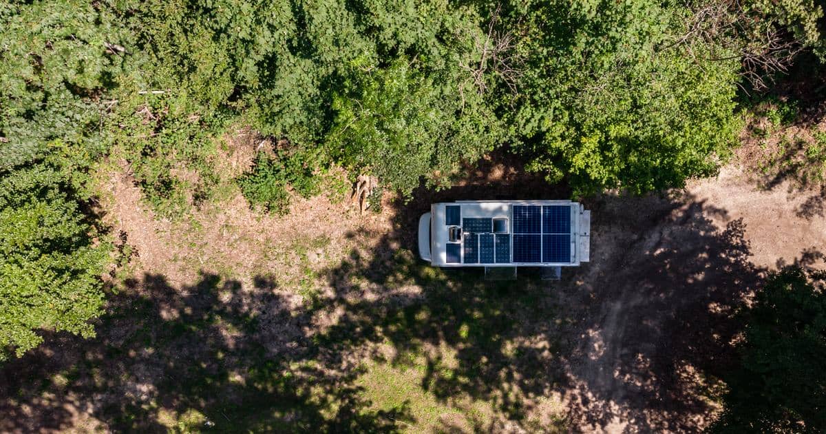 Vue aérienne d'un fourgon aménagé avec des panneaux solaires sur le toit, garé dans une clairière