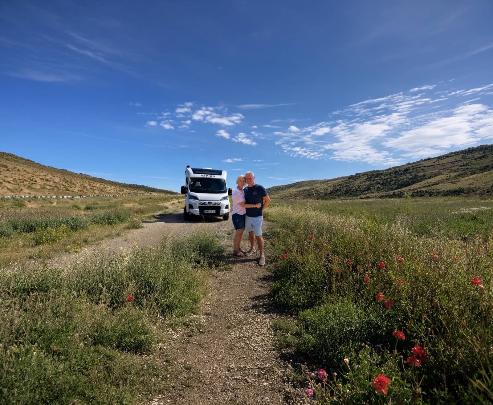 Un couple debout à côté de leur camping-car sur un chemin à travers des collines verdoyantes