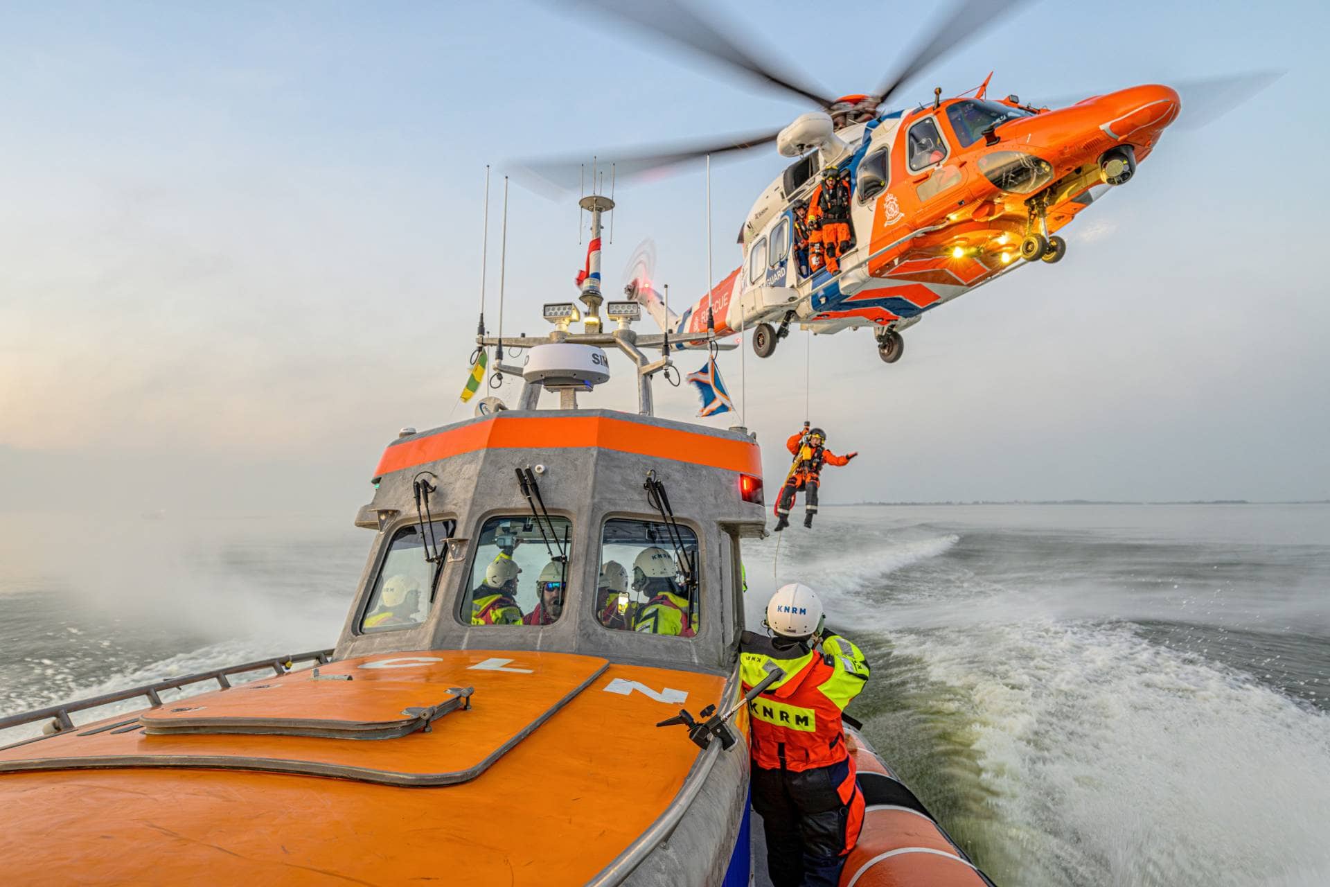 Navire de sauvetage de la KNRM en mer avec un hélicoptère de sauvetage hélitreuillant un membre d'équipage