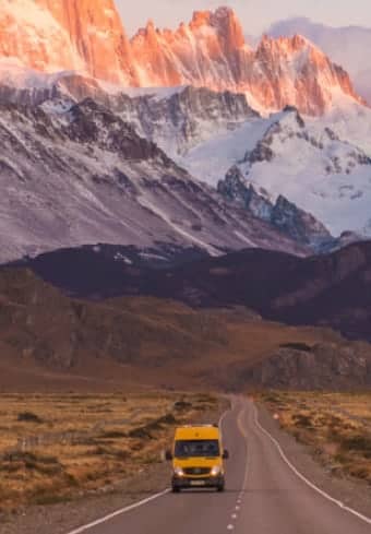 Fourgon aménagé jaune sur une route dégagée en dessous du massif enneigé du Fitz Roy en Patagonie